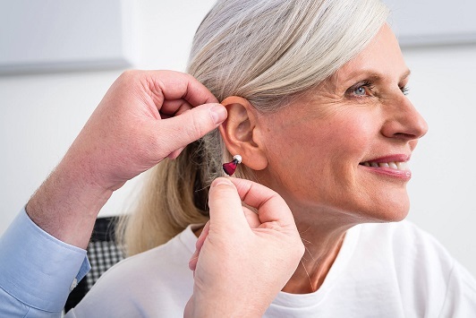 Ältere Frau bekommt ein modernes Hörgerät angepasst, Hörgeräteanpassung Senioren.